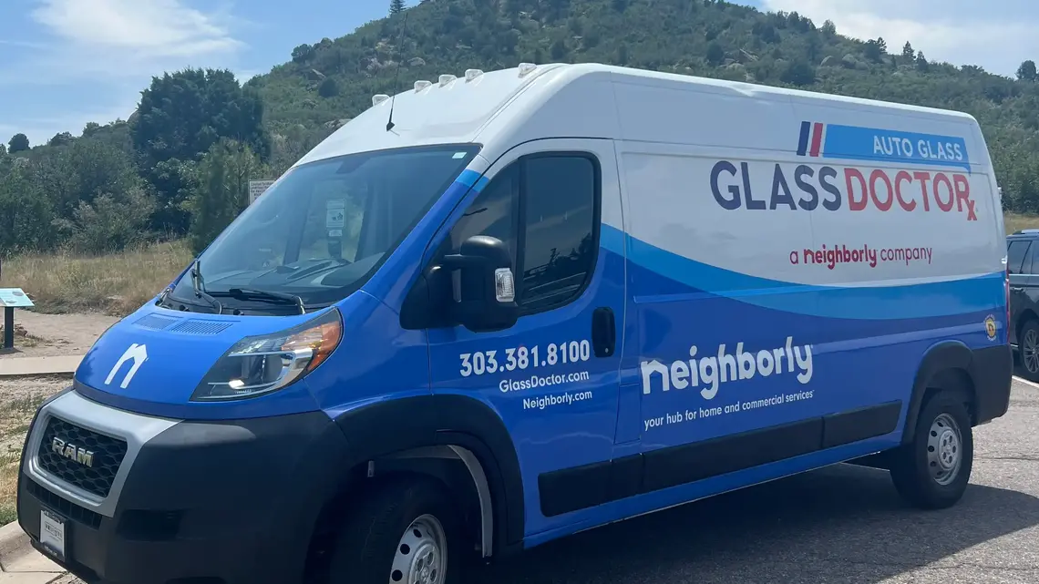 A close-up of a white, red, and blue Glass Doctor van with Castle Rock Mountain in the background.