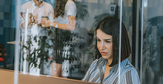 A picture of a woman sitting at a desk behind a sneeze guard.