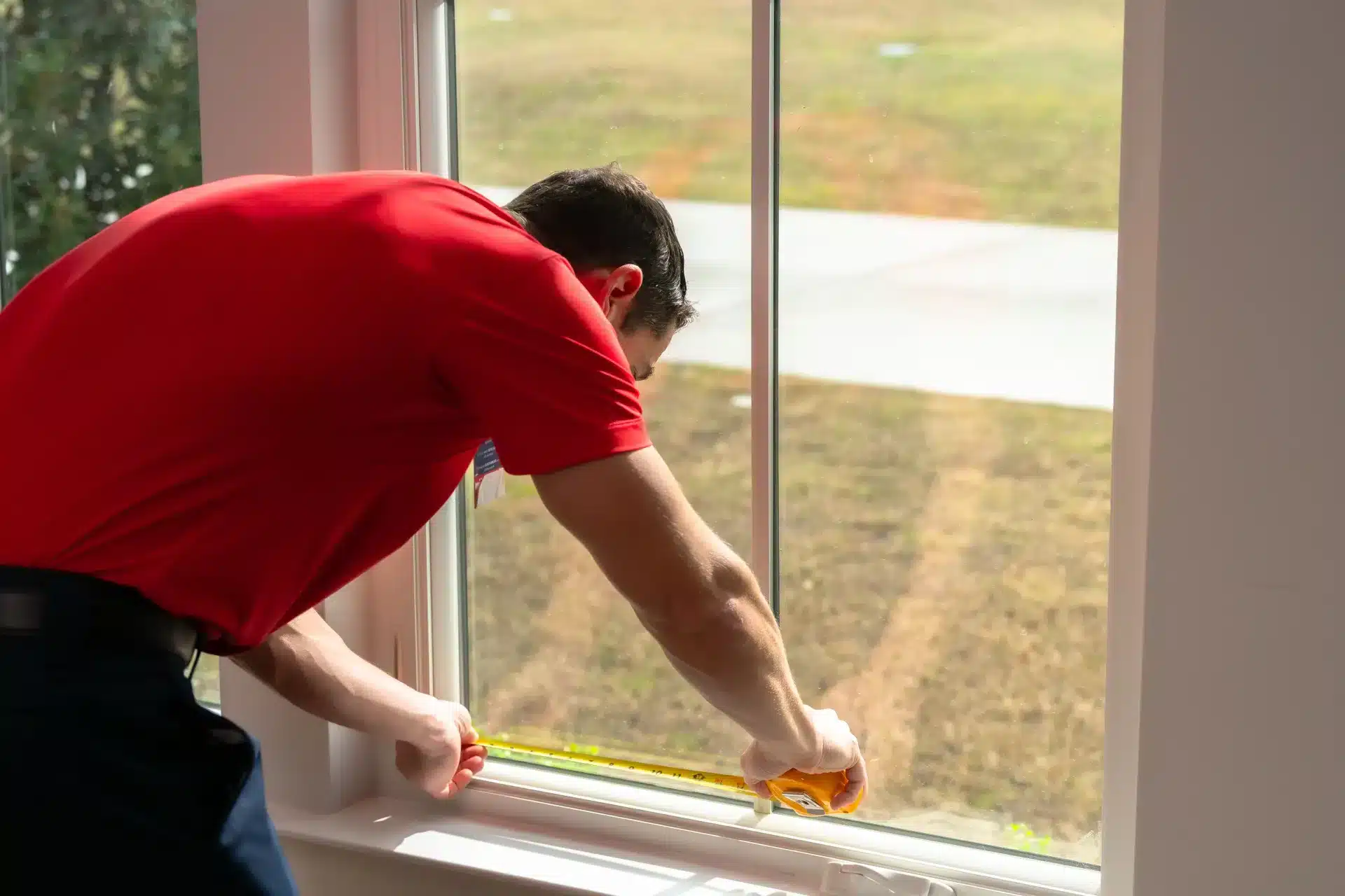 Glass Doctor technician measuring a window with a tape measure for home glass repair and replacement.