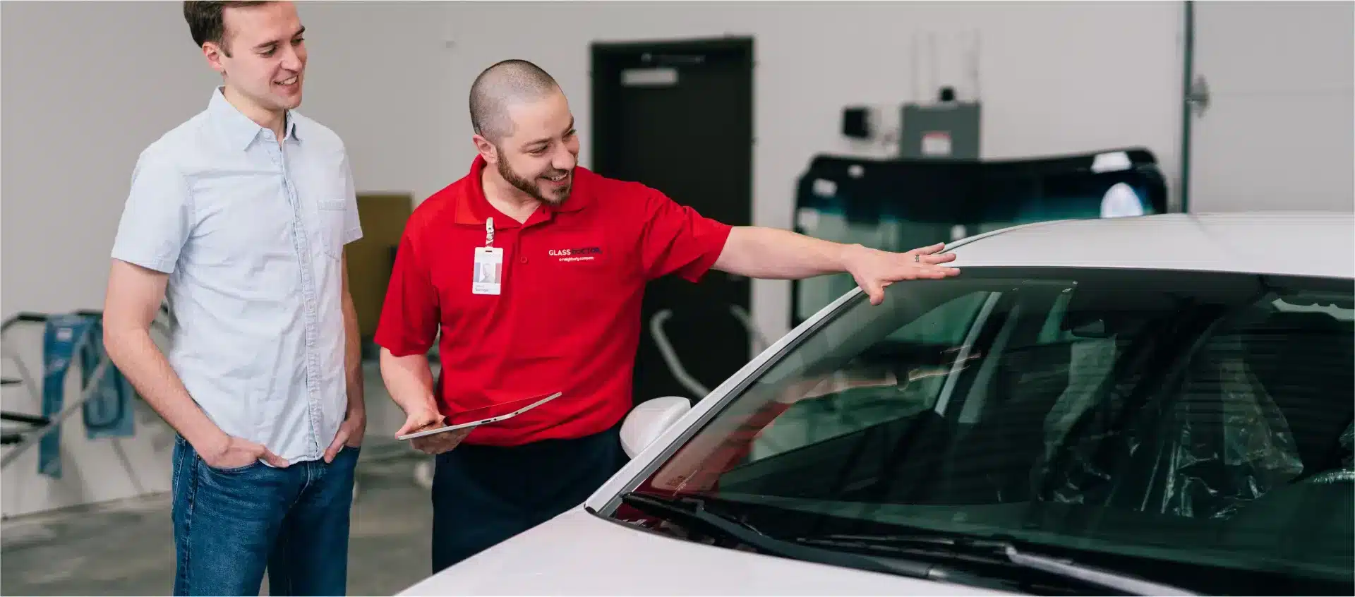 Auto glass repair and replacement technician assessing a cracked windshield with a customer.