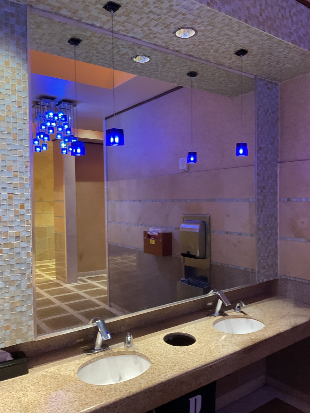 Large custom mirror installation above a dual-sink vanity in Pechanga Casino, Temecula, CA, reflecting pendant lighting and tiled interior walls.