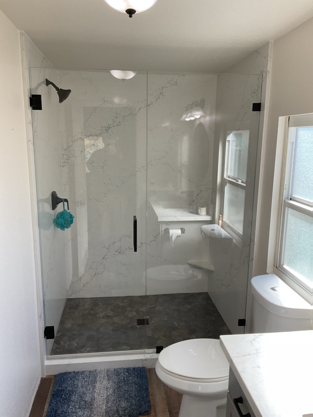 Frameless 2-panel glass shower enclosure with matte black hinges and handle, installed in a Murrieta bathroom featuring marble-style walls and dark stone tile floor.