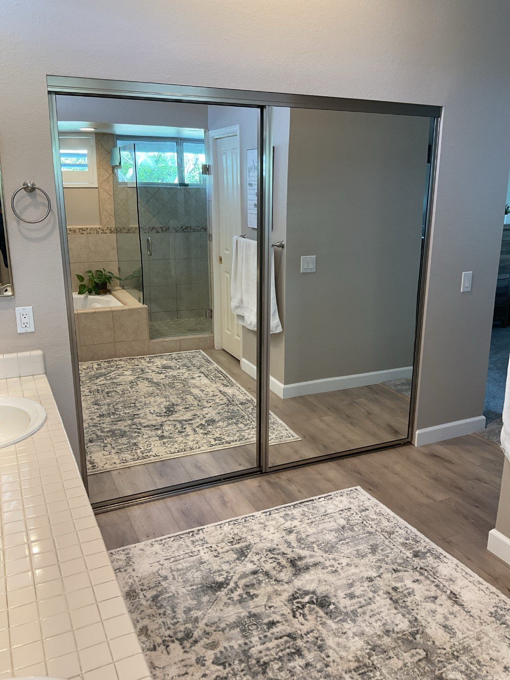 Sliding mirrored wardrobe doors installed in master bedroom, reflecting a bathroom with glass shower enclosure and tiled walls.