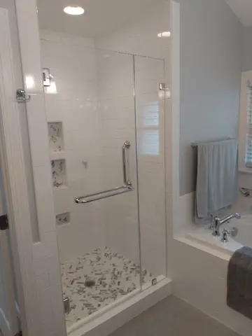 A frameless glass swing door with chrome towel bar and hardware on a white tile shower from Glass Doctor of Raleigh