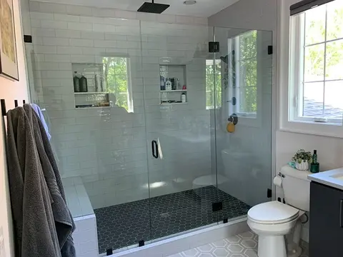 A glass shower enclosure with two frameless fixed panels and a swinging door in the middle on a white-tiled shower by Glass Doctor of Nashville.