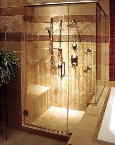 A shower with light brown tiles and a clear glass shower enclosure with a swinging door and a top frame.