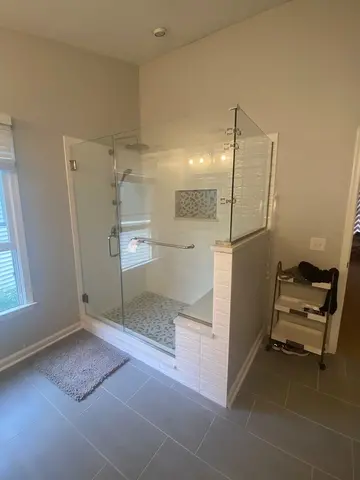A shower with white tile, a swinging glass door, and frameless glass panels on two sides with brushed nickel hardware