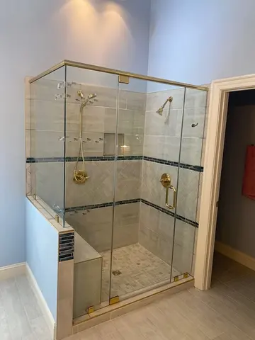 Satin brass hardware on a frameless glass shower swing door with a 90-degree angle by Glass Doctor of Raleigh