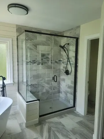 Semi-frameless glass shower with black hardware and a swinging door on gray tiles by Glass Doctor of Raleigh