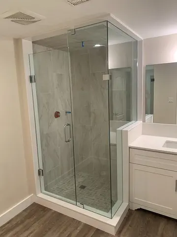 A grey tiled walk-in shower with a 90-degree frameless glass enclosure and chrome hardware by Glass Doctor of Newmarket.