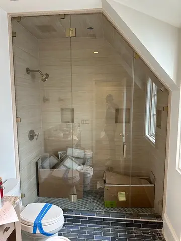 A fully-enclosed shower with an angled wall, floor-to-ceiling frameless glass panels and a swinging door by Glass Doctor of Nashville.