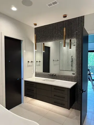 A mirror with back-lighting on a black tiled wall above a white countertop installed by Glass Doctor of Nashville.