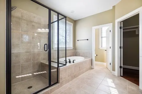 A large bathroom with a shower enclosed in clear glass and black metal frame.