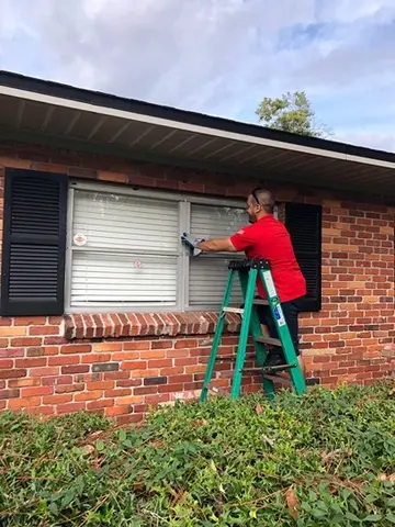 A Glass Doctor of Tampa Bay service professional standing on a ladder and repairing the window of a house. 
