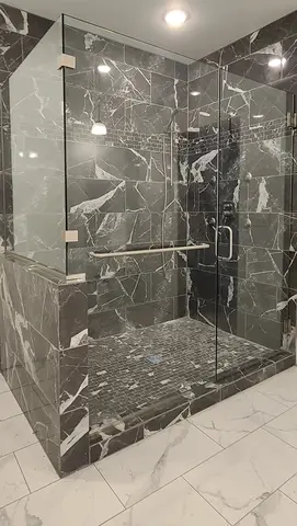 A shower with black and white marbled tiles and a frameless clear glass enclosure with swinging door.