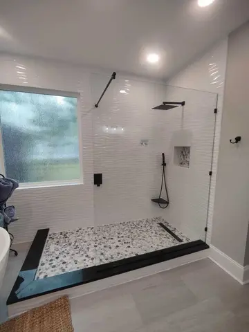 A shower with white textured tile and a frameless clear glass splash panel with black hardware by Glass Doctor Home + Business of Myrtle Beach.