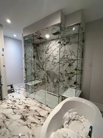 A custom shaped frameless glass shower enclosure surrounding a marble tile shower with two seats installed by Glass Doctor of Barrie, ON.