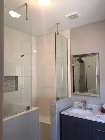 A walk-in shower with half walls and fixed frameless glass panels on either side of entrance by Glass Doctor of York Region.