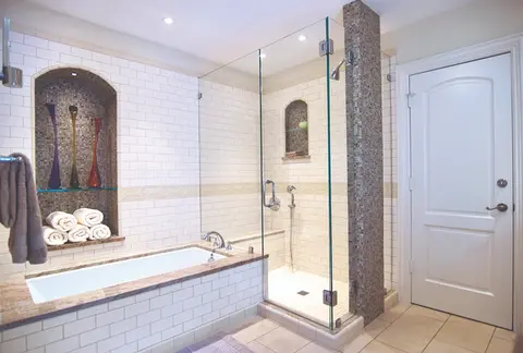 A bathroom with white subway tiles and a tub next to a shower enclosed with frameless glass panels and chrome hardware.