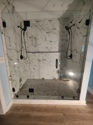 A three frameless glass panel shower enclosure with black hardware on a white marble shower installed by Glass Doctor Home + Business of Myrtle Beach.