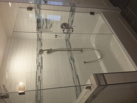 Angle one of a frameless glass shower door installed on a tub with white subway tiles and gray accent tiles by Glass Doctor of Sarasota.