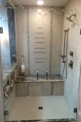 Frameless double swinging shower doors with a shaped top edge on a tiled shower with a phrase written on the wall.