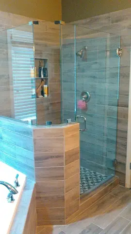 A tan tiled shower with an angled half-wall on one side topped with frameless glass splash panels and a full-height frameless glass door by Glass Doctor of Nashville.