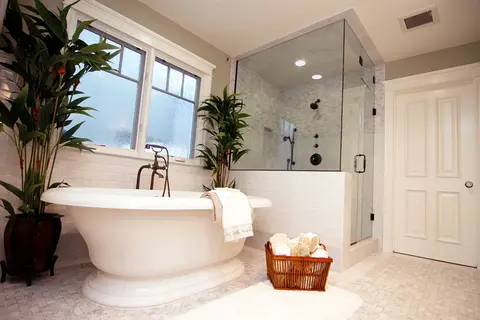 A white bathroom with a tub and a shower with a clear frameless glass enclosure featuring black hardware.