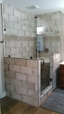 A shower enclosure with two half-walls topped with frameless glass splash panels and a frameless glass door between them by Glass Doctor of Nashville.