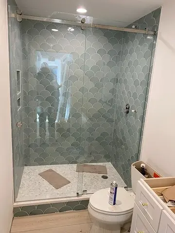 A sliding frameless glass door installed by Glass Doctor of Nashville on a shower with tiles that look like fish scales.