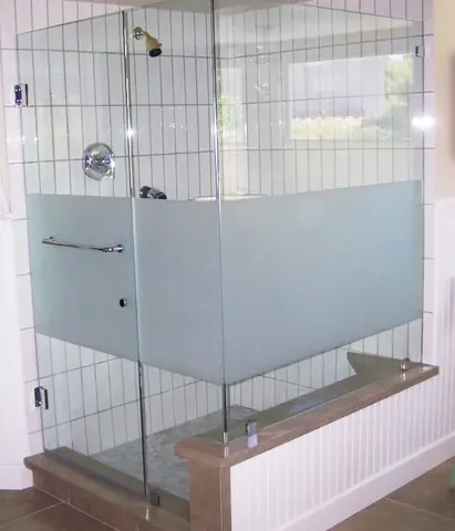 A frameless shower enclosure with a strip of sandblasted glass across the middle on a white tile shower.