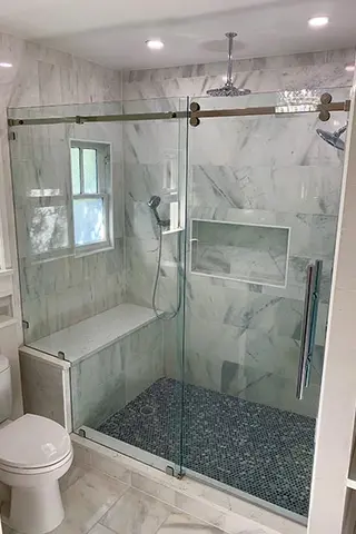 A shower enclosure with white and gray marble tiles, a bench, and a glass panel with sliding door enclosure.