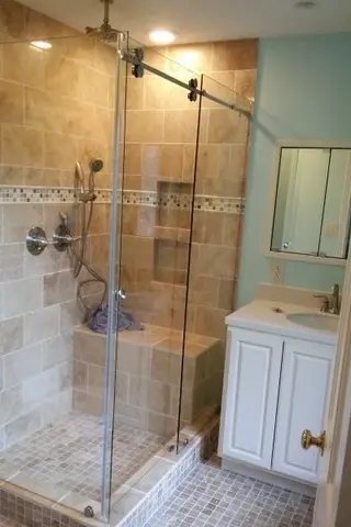 A brown tiled shower with a 90-degree frameless glass enclosure and sliding door.