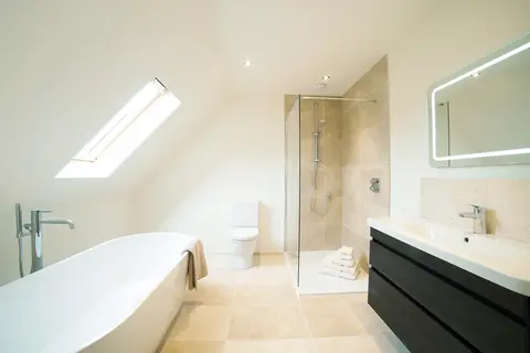 A beige tile shower in a white bathroom with a frameless clear splash panel.