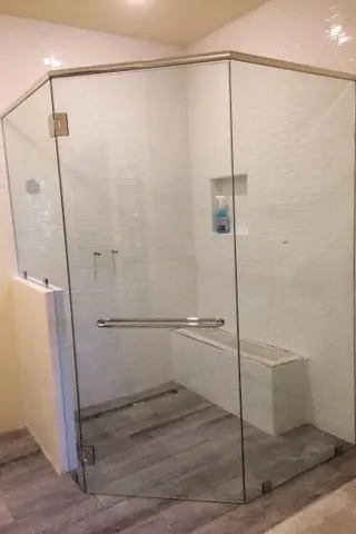 A shower enclosure with white subway tiles and a bench enclosed with a three-panel frameless glass enclosure and a diagonal panel.