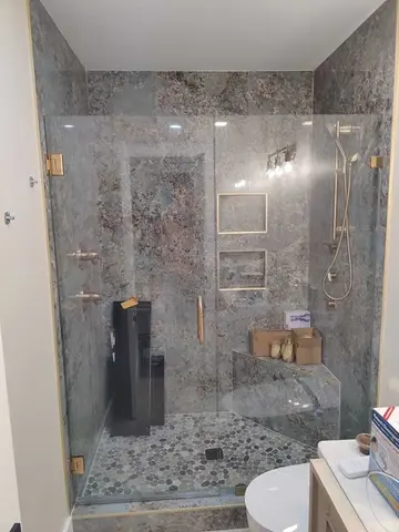 Gold hardware on frameless glass panels with a swinging door on a tile shower by Glass Doctor Home + Business of Myrtle Beach.