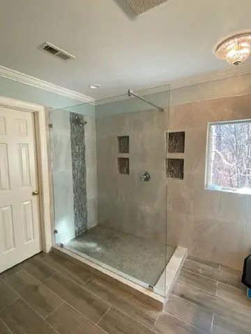 A beige tile shower with a frameless glass splash panel and a wall mount support bar from Glass Doctor of Raleigh