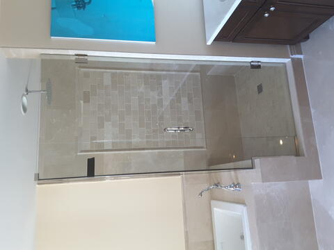 A shower with beige tiles and a frameless clear glass enclosure and swinging door installed by Glass Doctor of Ocala.