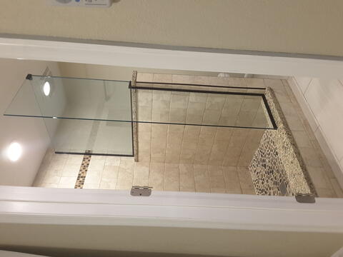 Frameless glass splash panels installed by Glass Doctor of Pinellas County on an open shower stall with tan tiles.