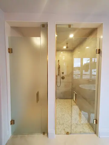 Frosted and clear frameless glass shower doors with gold hardware installed on side-by-side entrances by Glass Doctor of York Region.