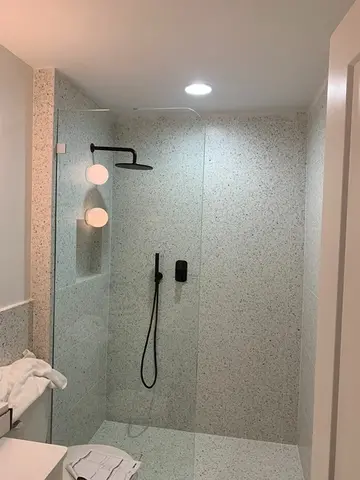 A stone-tiled shower with black hardware and a frameless glass splash panel with a rounded top corner installed by Glass Doctor of Nashville.