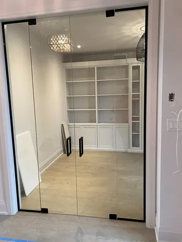 A semi-frameless glass wall with double swinging doors and black hardware installed on the entrance to an office by Glass Doctor of York Region.