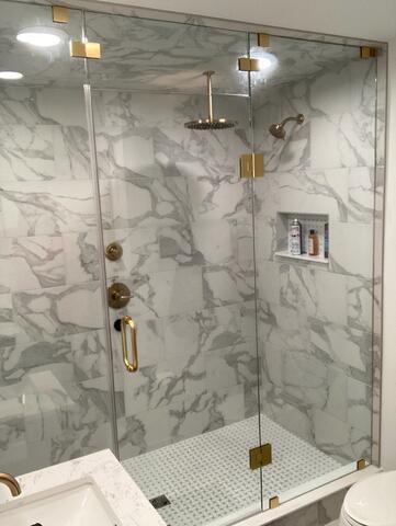A custom walk-in shower with gray tiles and gold fixtures and a frameless glass shower door with gold hardware installed by Glass Doctor of Sarasota.