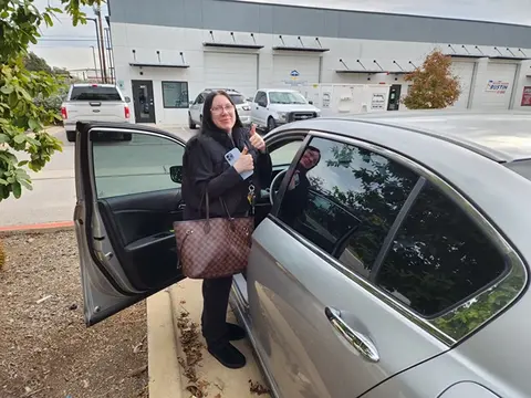 A satisfied customer of Glass Doctor Auto of Cedar Park gives two thumbs up in front of her silver car.