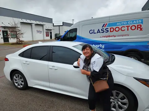 A happy customer poses in front of her white car with a Glass Doctor Auto of Cedar Park truck in the background.