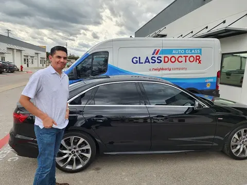 A happy customer poses in front of his black car with a Glass Doctor Auto of Cedar Park truck in the background.