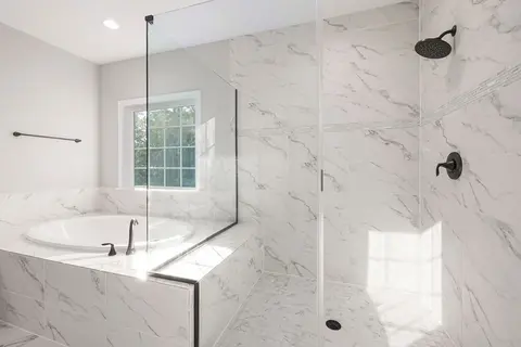 A marble-tiled shower with clear frameless glass enclosure next to a raised tub.