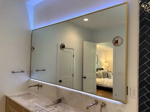 A bathroom mirror over a double-sink vanity with a gold frame, back-lighting, and three round cutouts for light fixtures by Glass Doctor of Nashville.
