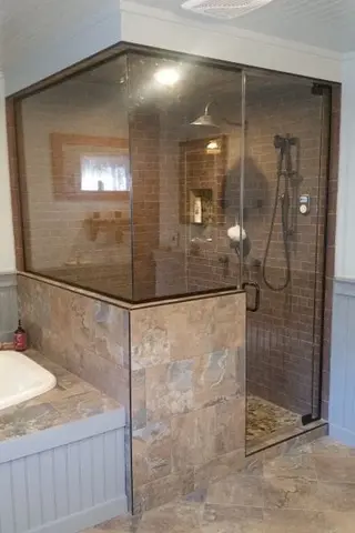 A glass enclosed shower with brown marble tiles on the outside and red brick tiles on the inside.