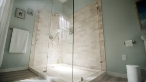 Green bathroom with beige tiled shower and a frameless clear glass shower enclosure.